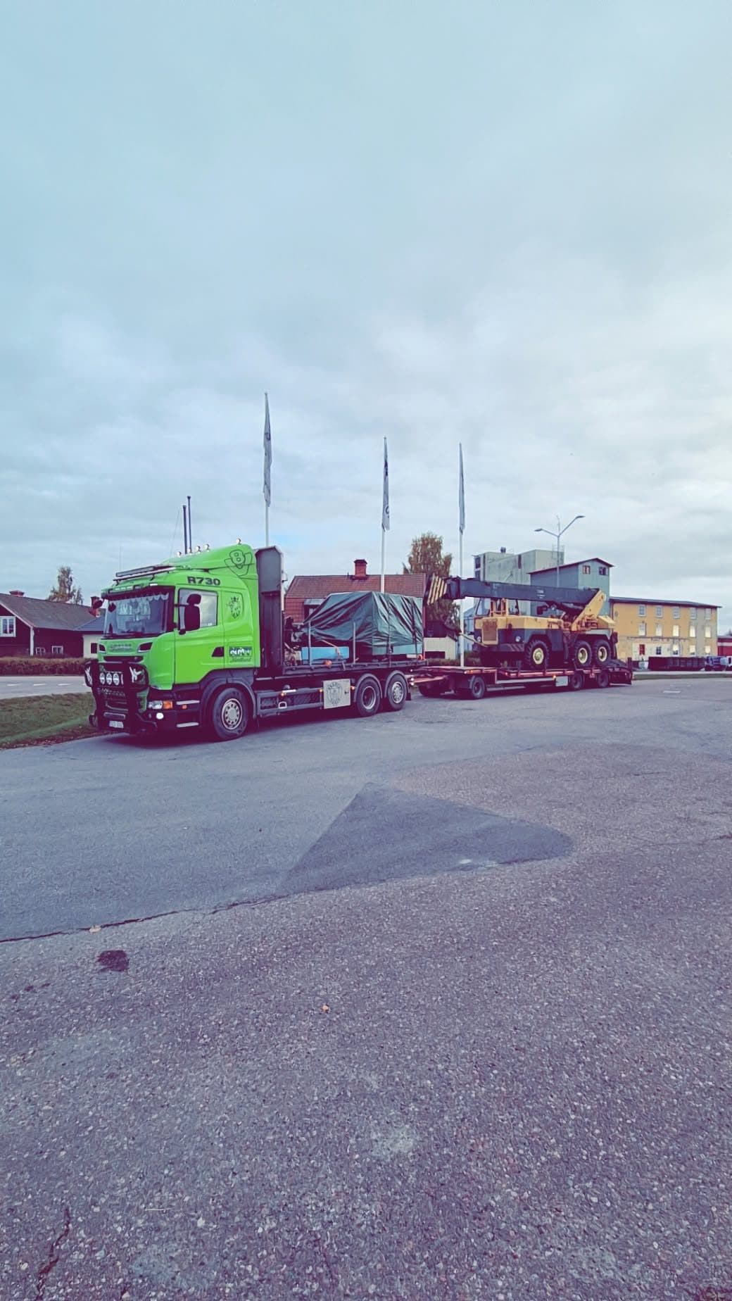 Ekipaget vid en industrigård med presenningstäckt last på flaket och en gul maskin på släpet