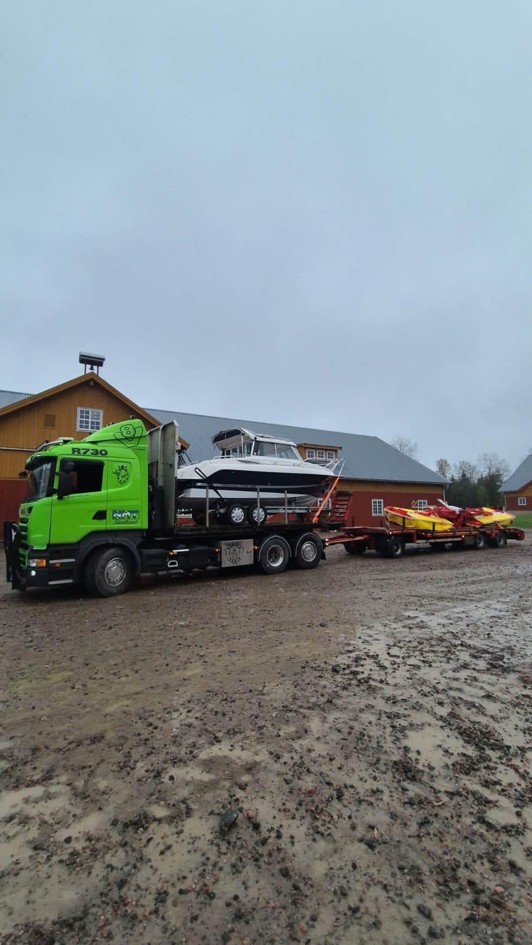 Scanian R730 med en motorbåt på flaket och fritidsbåtar på släpet, vid en röd gård