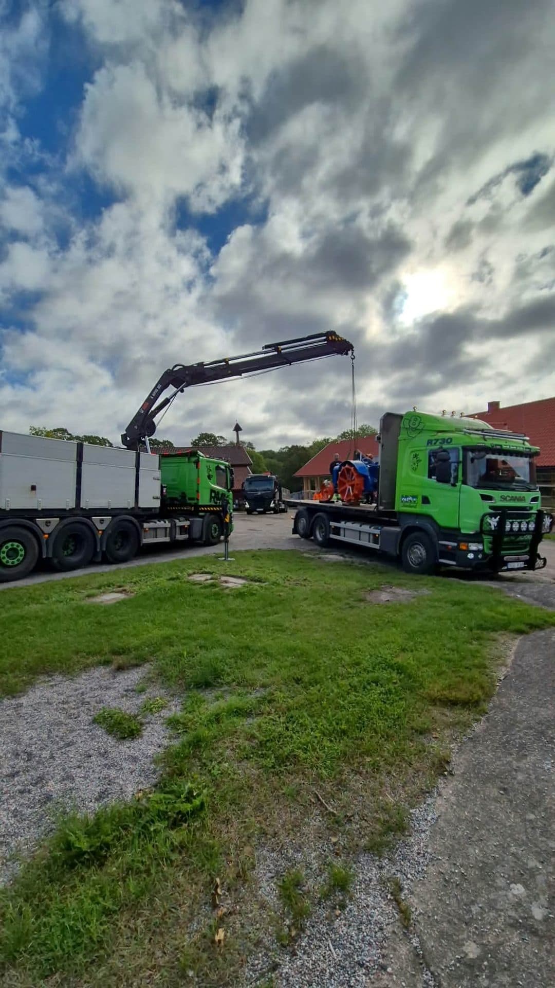 En kranbil lyfter en äldre traktor upp på Scanians flak vid en gård